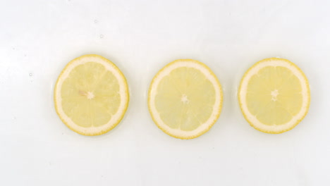 Slow-motion-water-splash-on-three-slices-of-lemon-lying-on-a-white-background-in-water